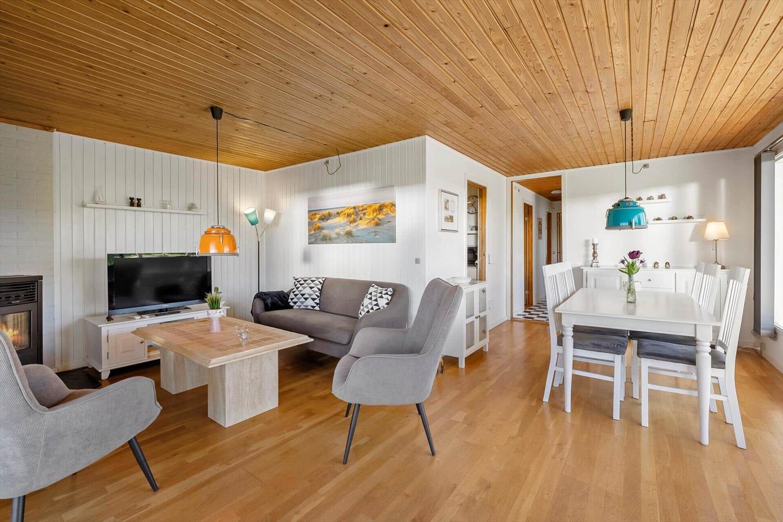 Living and dining area with hardwood floor, white wall paneling, and wood ceiling. Furniture in gray and white.