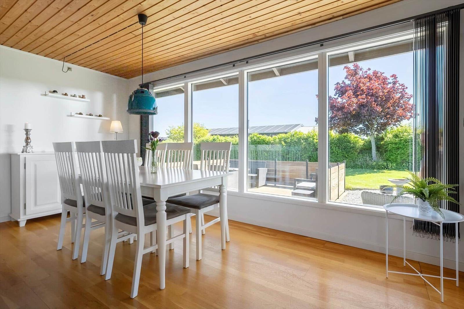Dining room with white table, chairs, and large window view of garden.