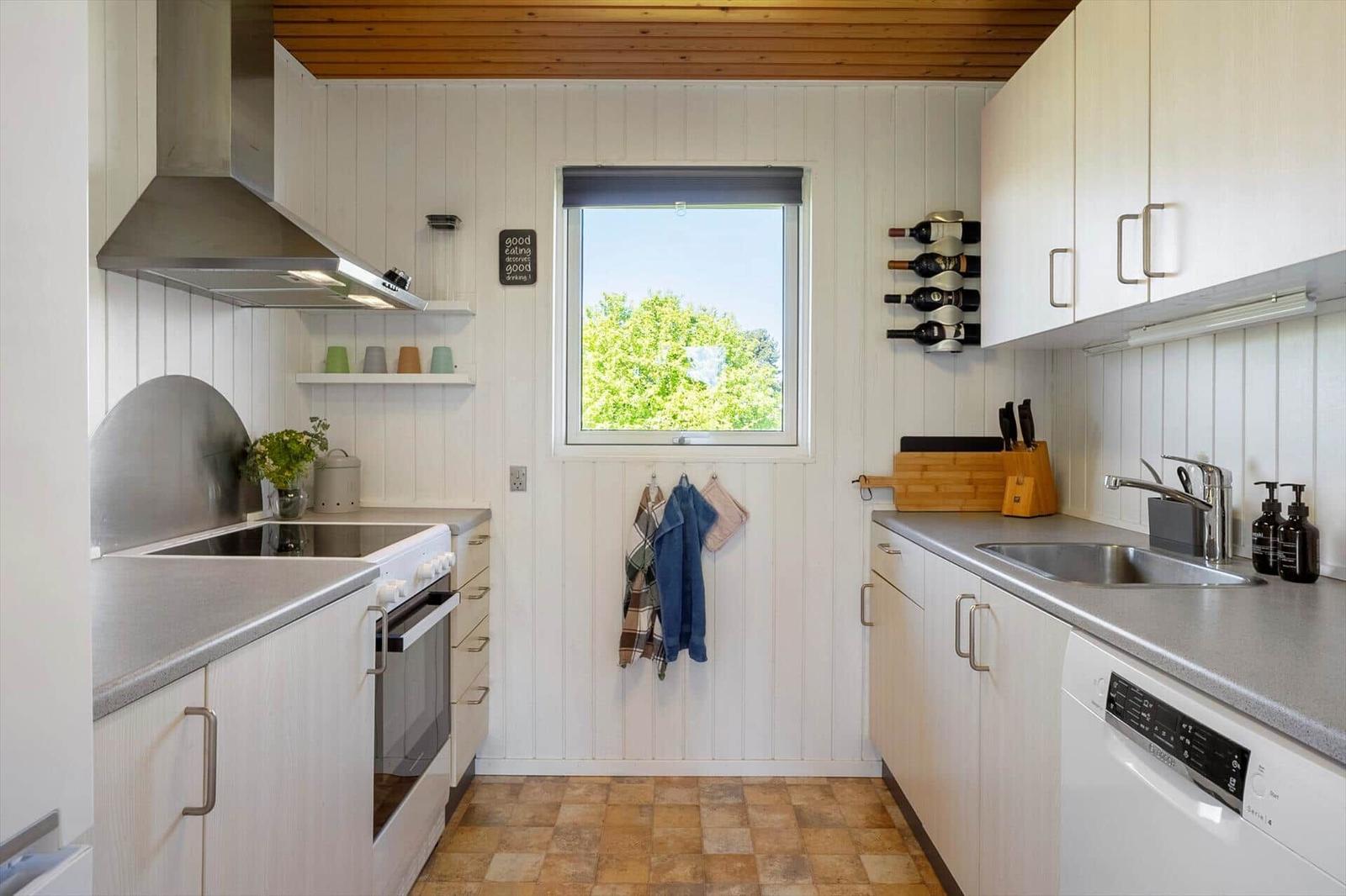 Kitchen with white cabinets, stainless steel sink, and window overlooking trees.