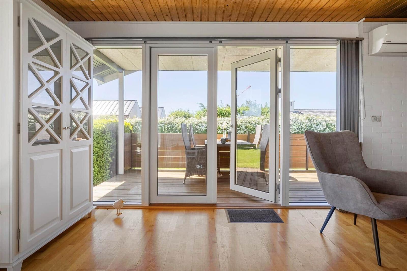 Bright terrace with table and chairs. Wooden floor and white sliding doors.