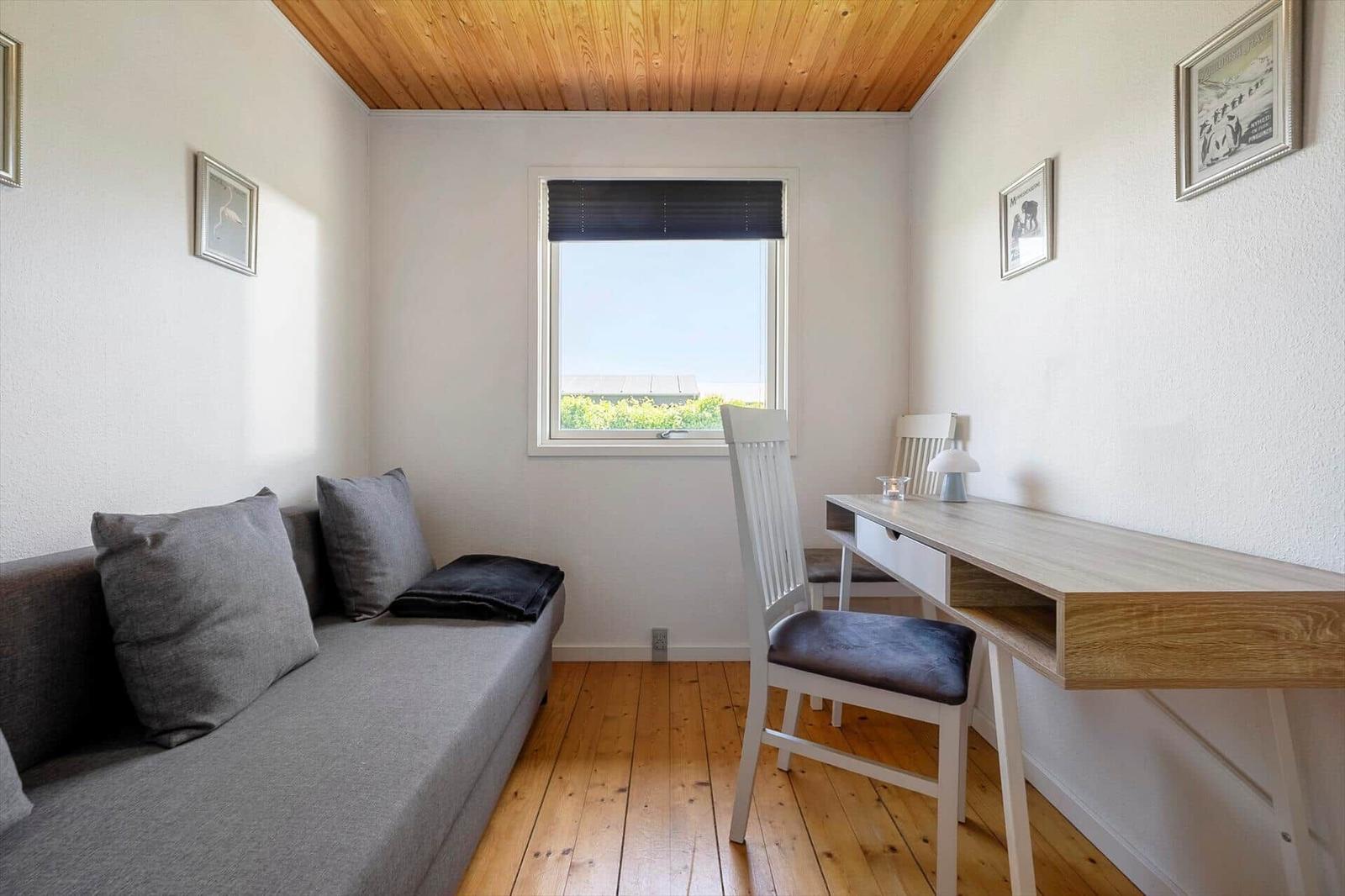 A room with sofa, desk and window. Wooden ceiling and floor.
