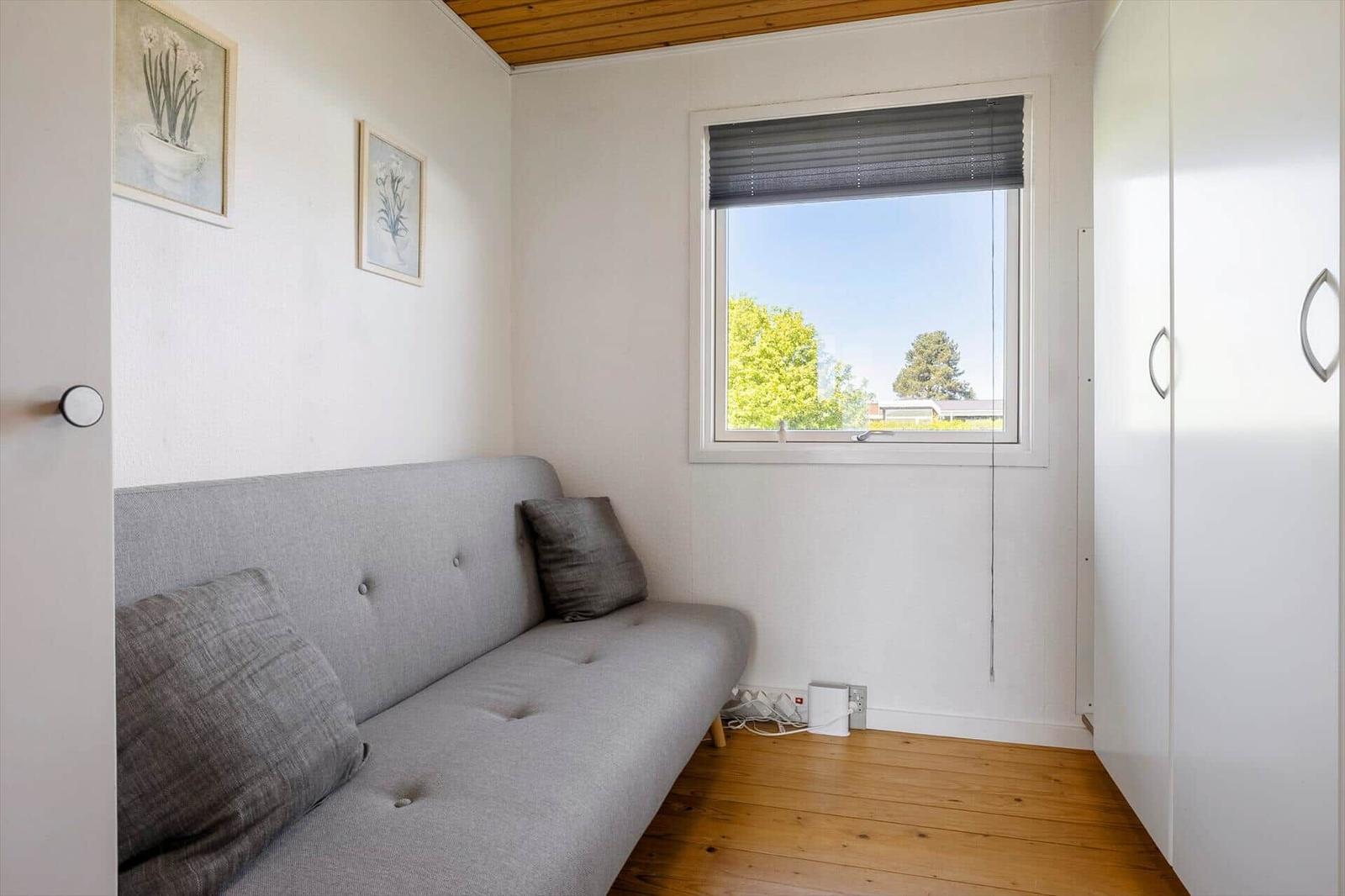 A room with gray sofa, window and white walls. Wooden floor and wardrobe.