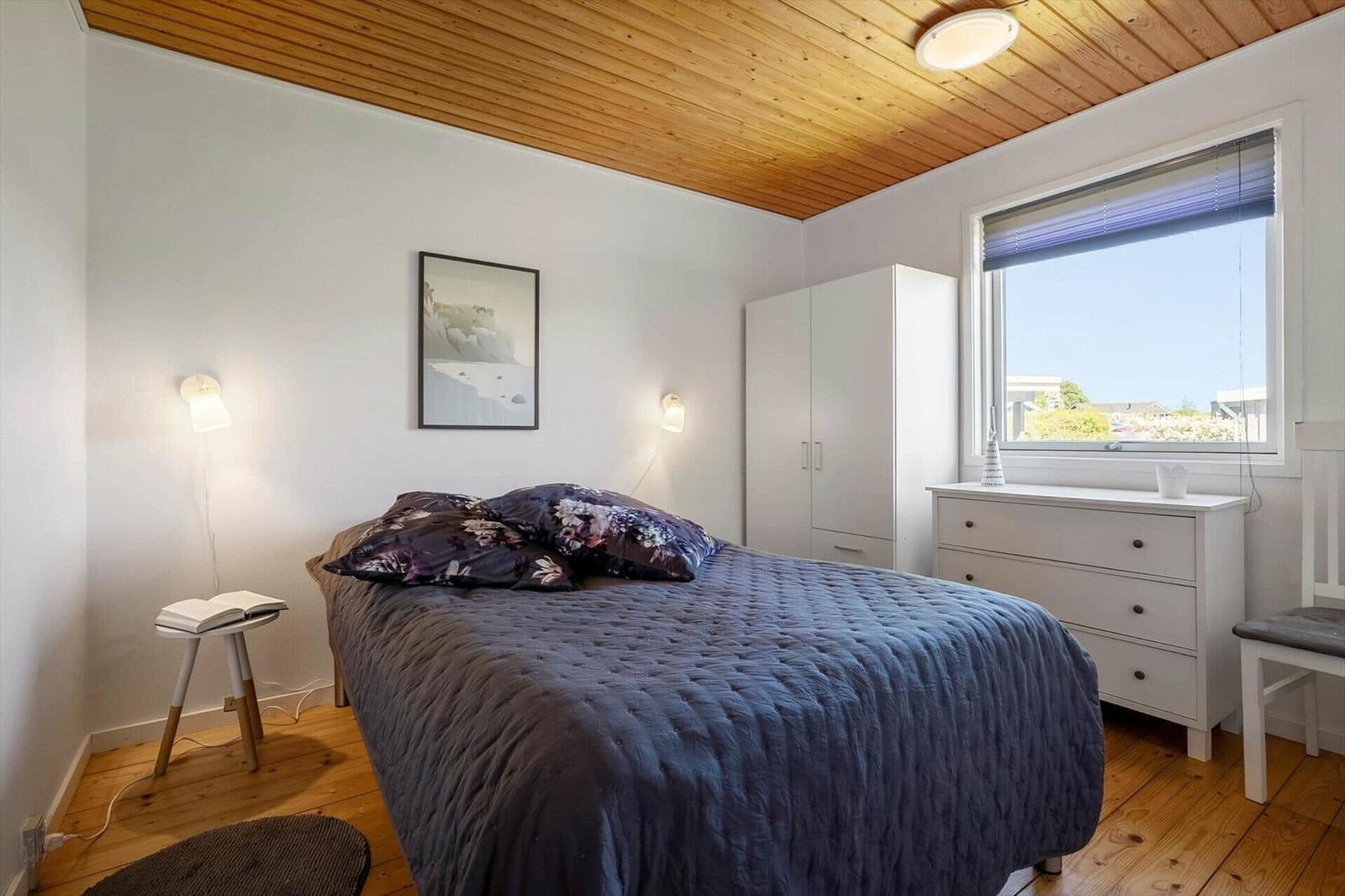 Bedroom with bed, wardrobe, and window. Wooden ceiling and floor.