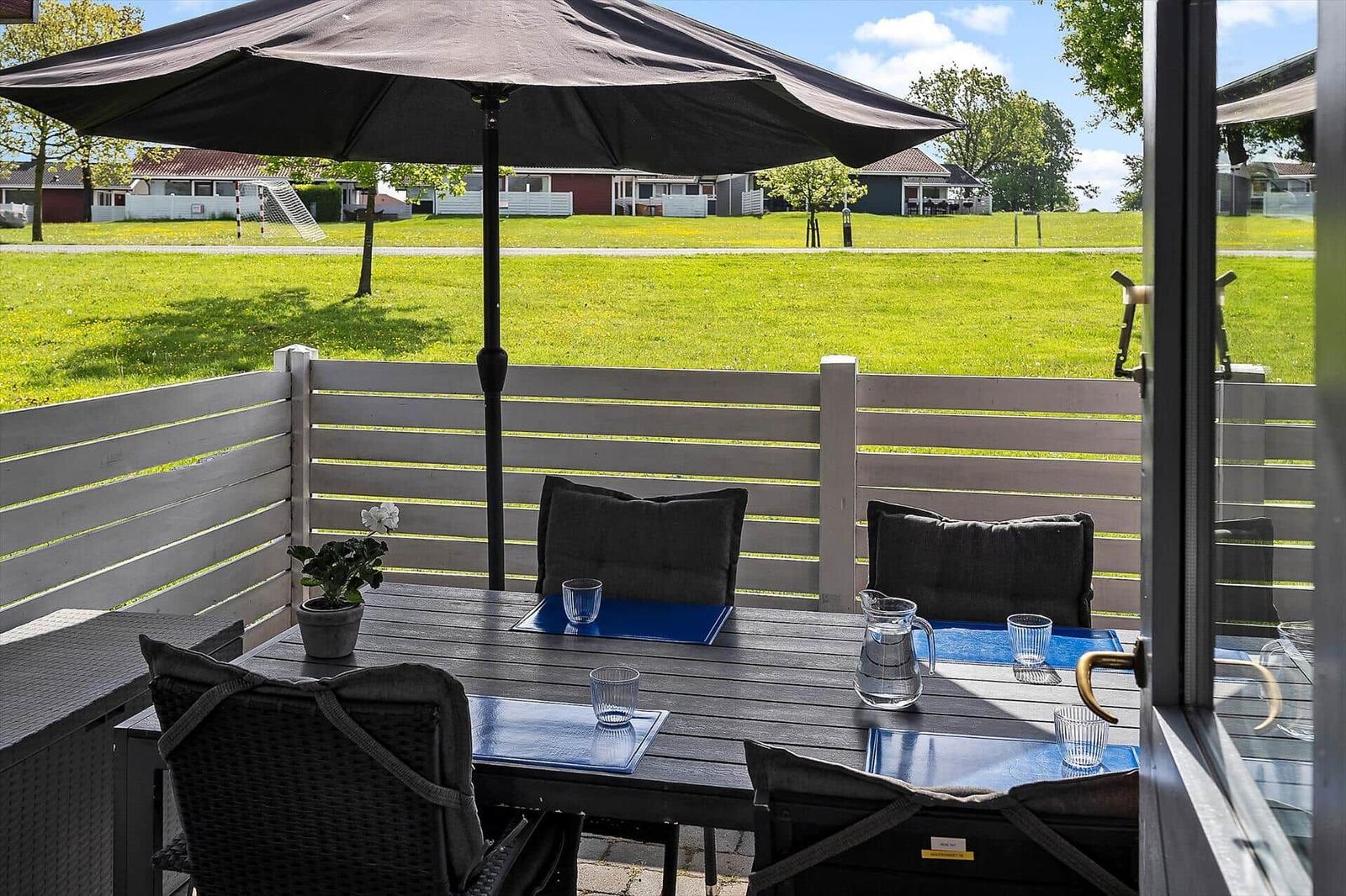 Terrace with table, chairs, and umbrella. View of green lawn and houses in the background.