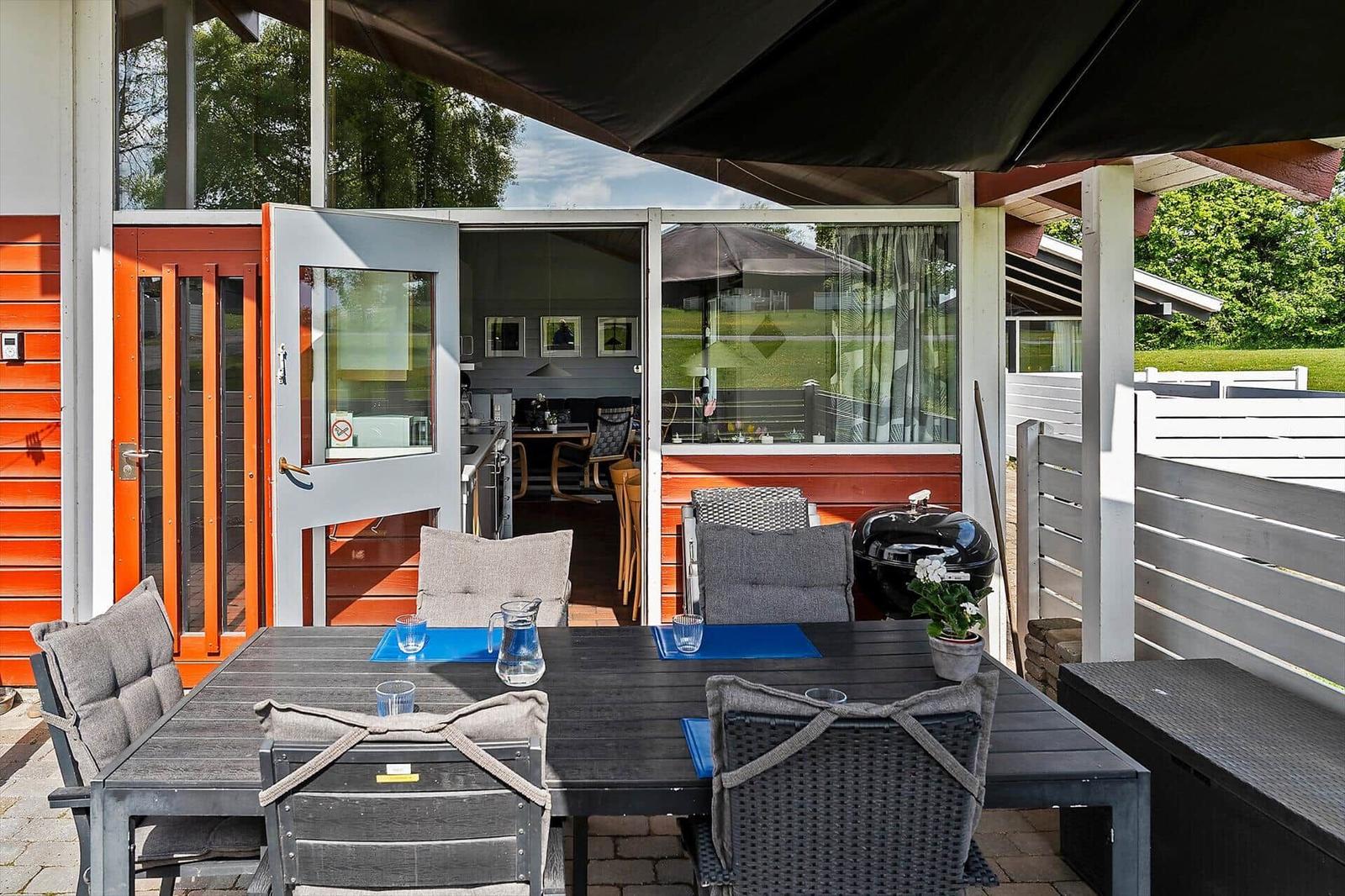Terrace with table, chairs, and grill under awning. View into house through glass doors.