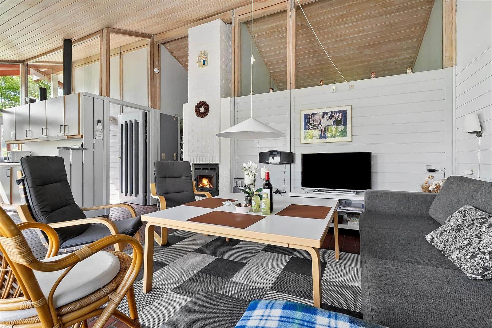 Living room with fireplace, sofa, dining table, and kitchen area in background.