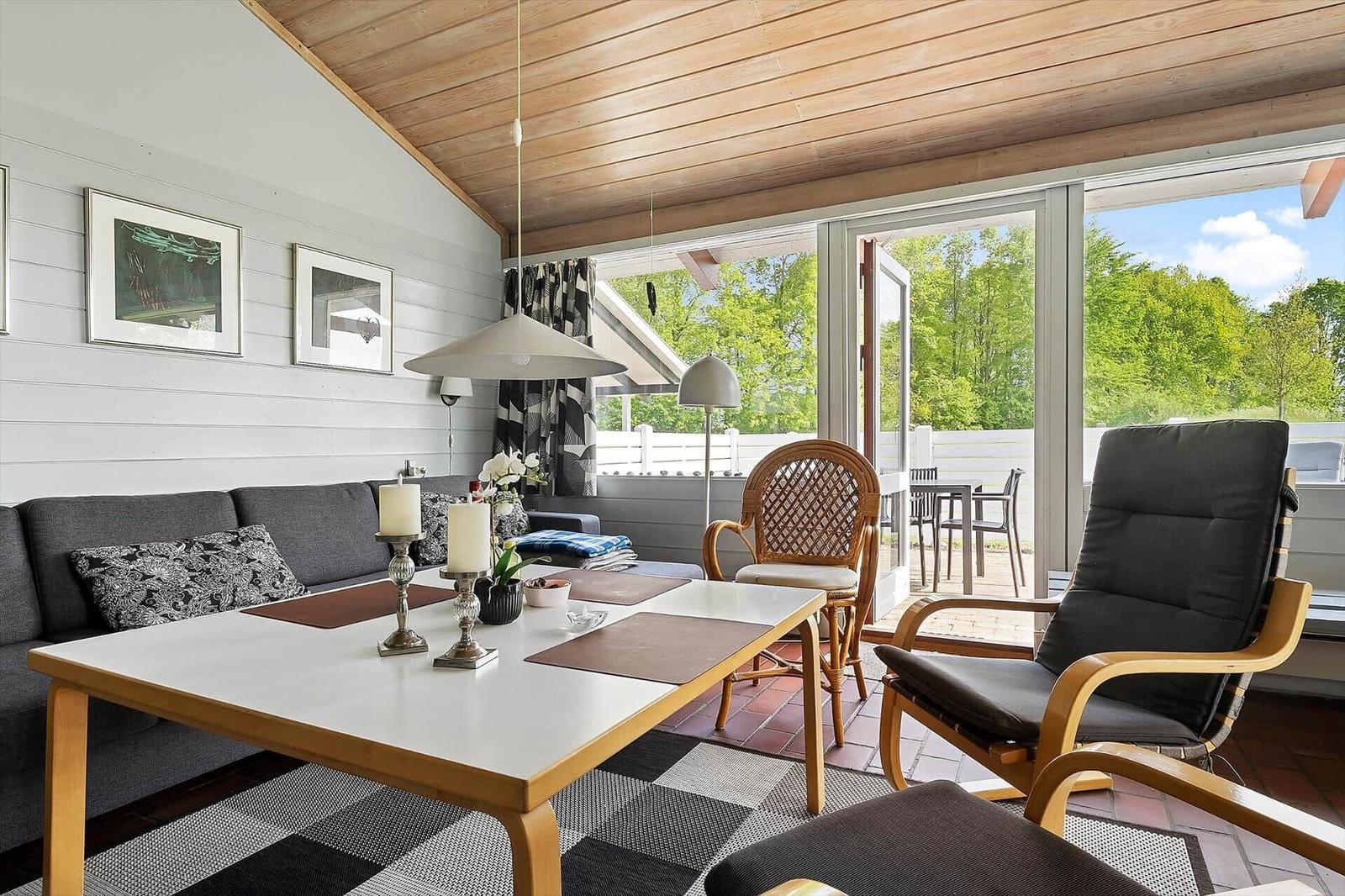 Living area with sofa, table, and chairs. Passage to terrace with view of trees.