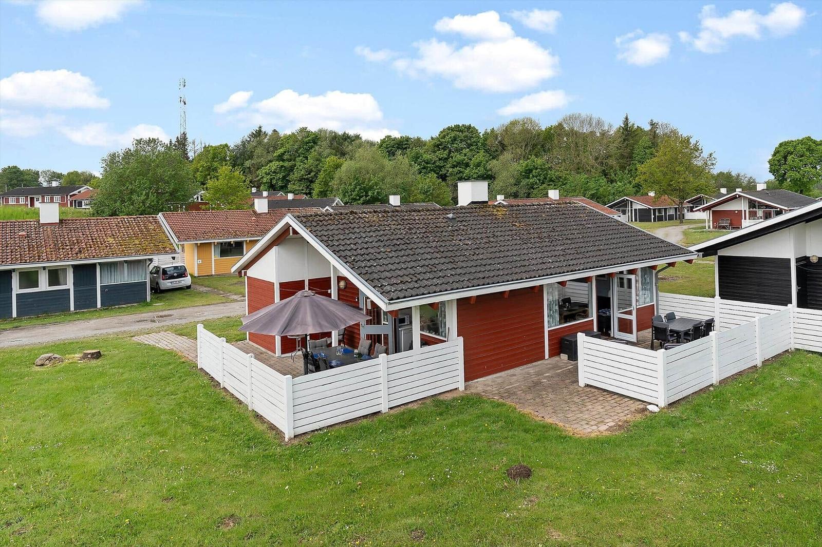 Red vacation home with terrace, garden, and seating under umbrella.