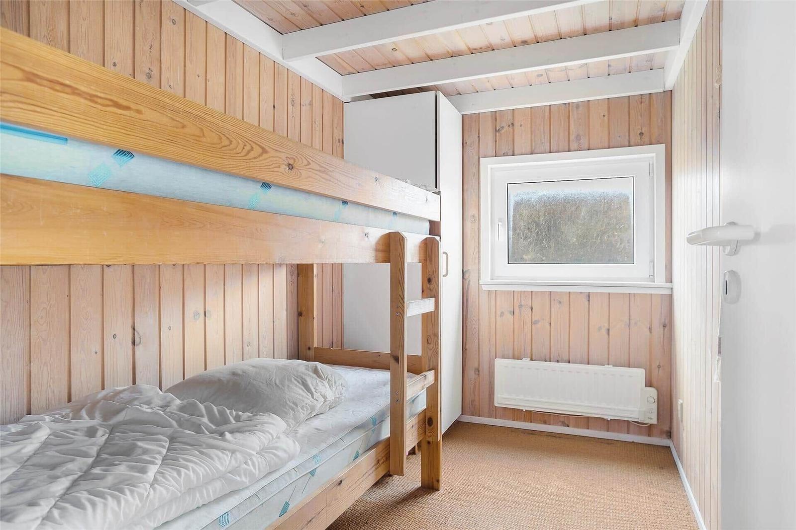 Ein Raum mit einem Doppelstockbett, Holzwand und Fenster.