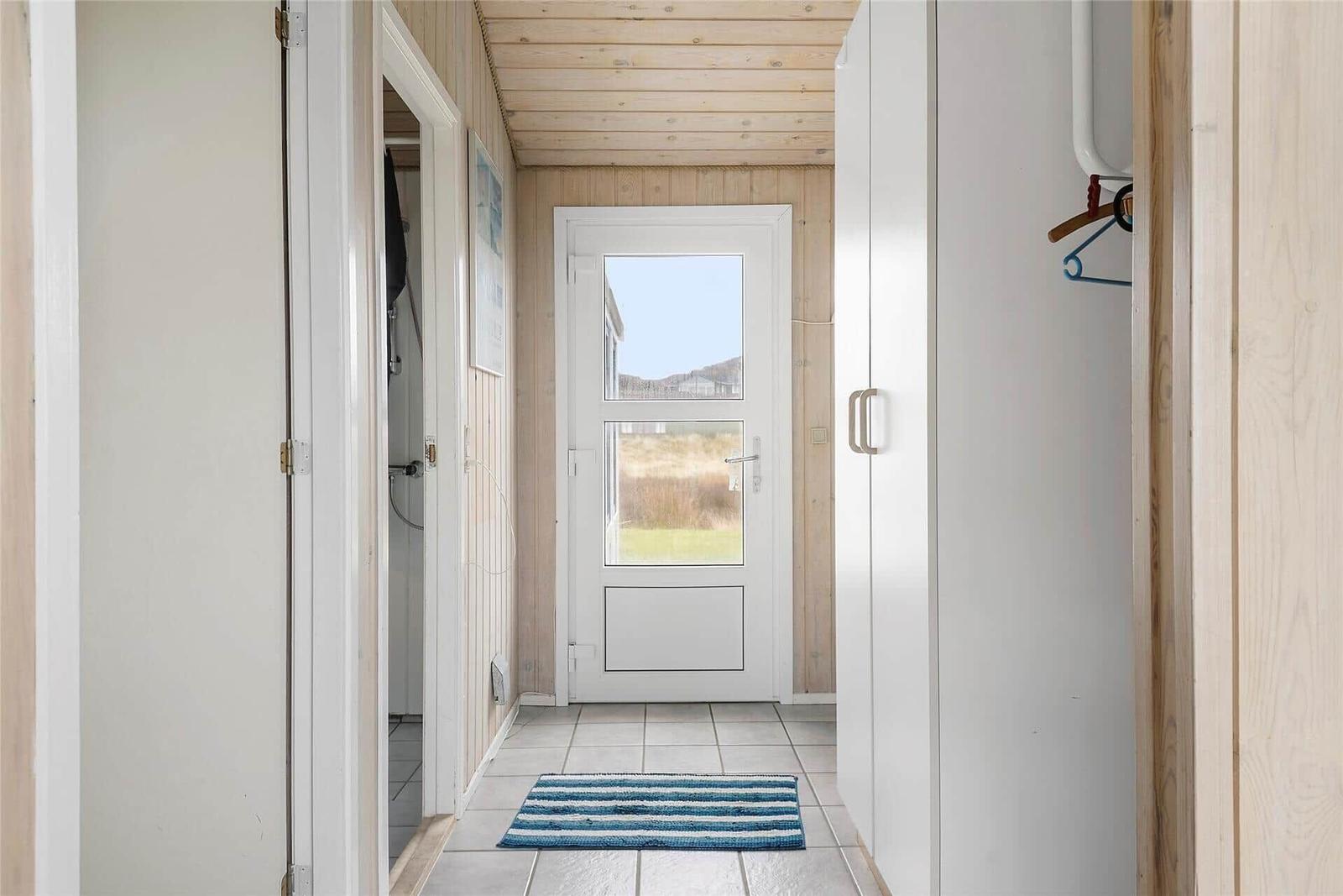 Flur mit weißen Schränken, Holzdecke und Tür zum Außenbereich.