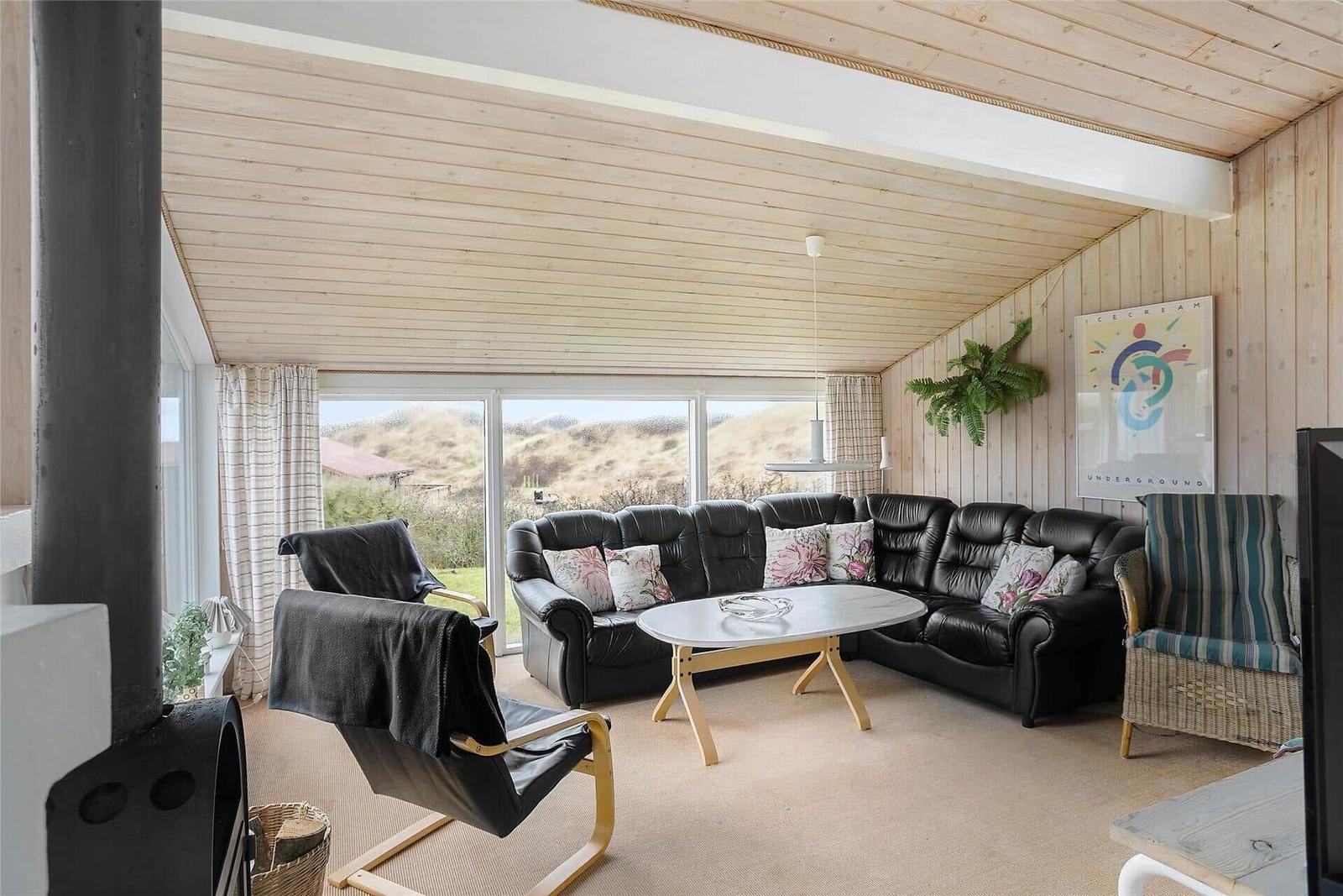 Wohnzimmer mit schwarzer Ledercouch, Holztisch und Blick auf die Landschaft.