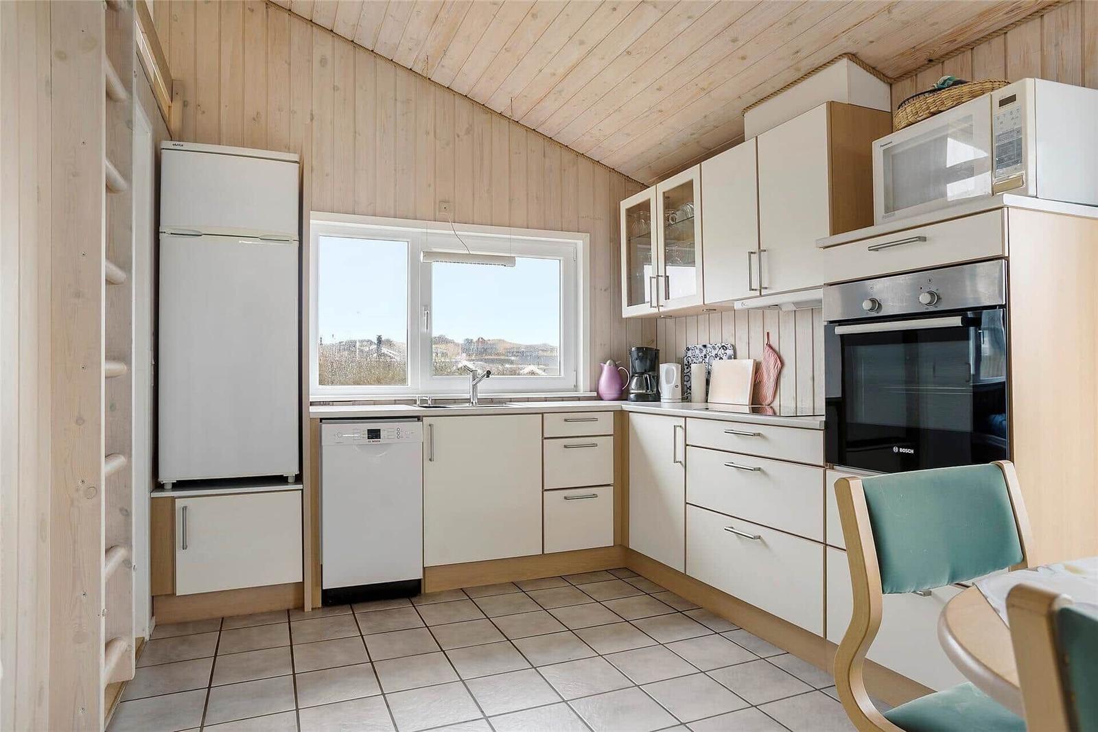 Küche mit Kühlschrank, Spülmaschine und Herd. Holzwände und Fenster mit Blick.
