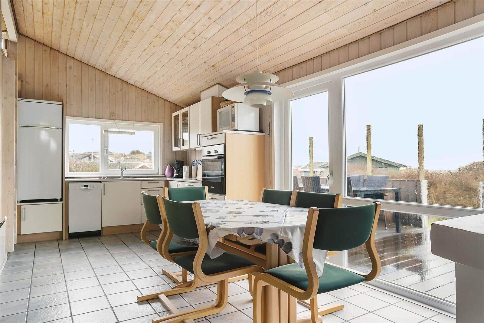 Küche mit Esstisch und grünen Stühlen. Große Fenster und Holzdecke.