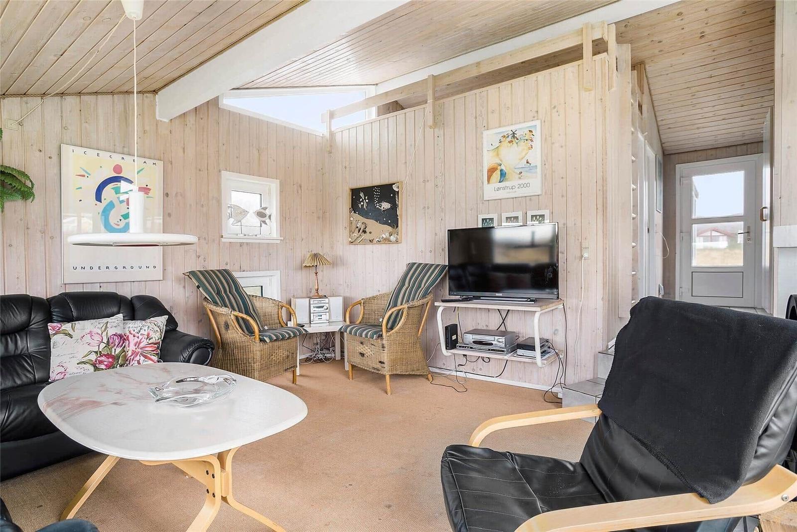 Wohnzimmer mit Holzwänden, Sofa, Stühlen und Fernseher.