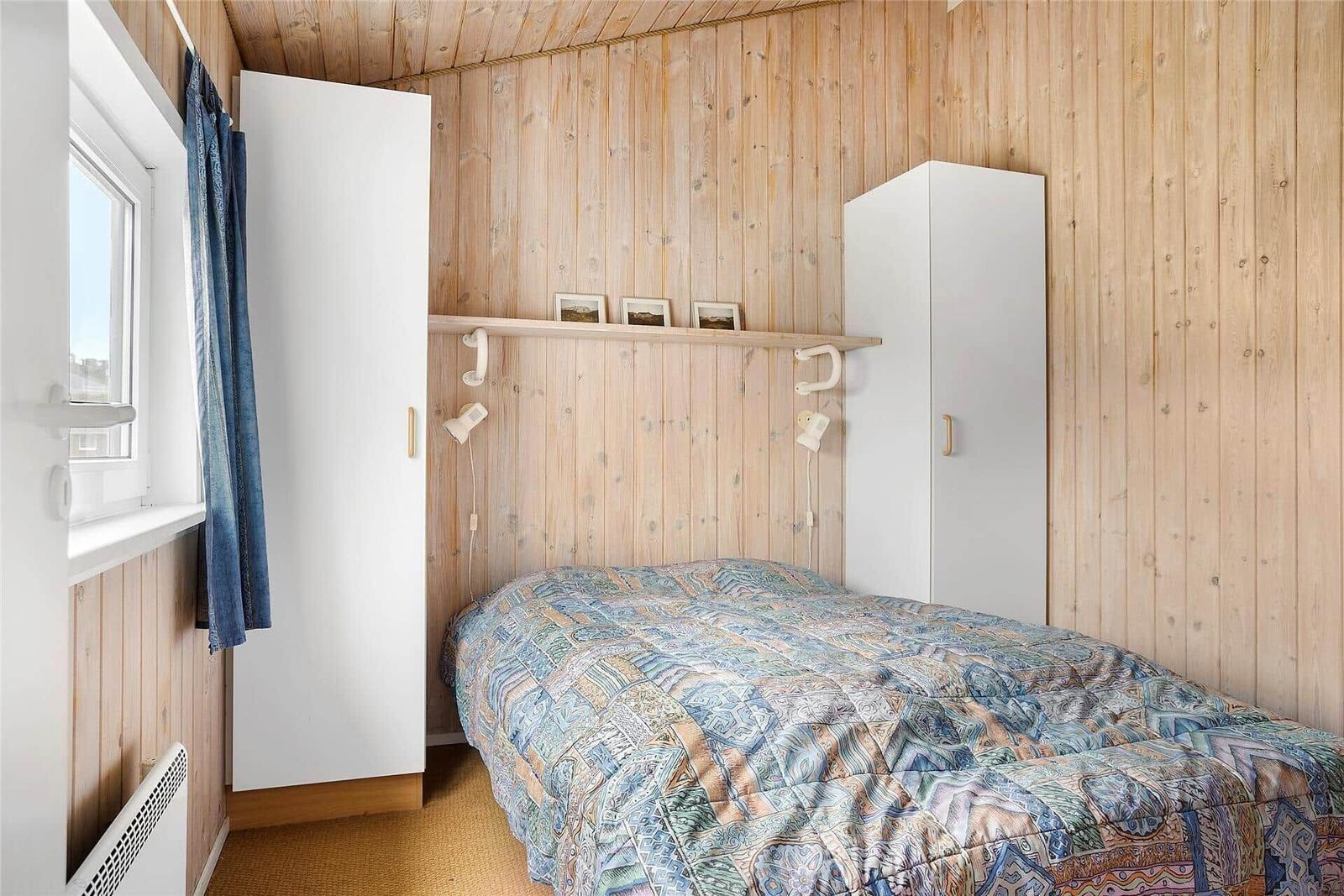 Schlafzimmer mit Holzwand, Bett, weißen Schränken und Fenster mit Vorhang.