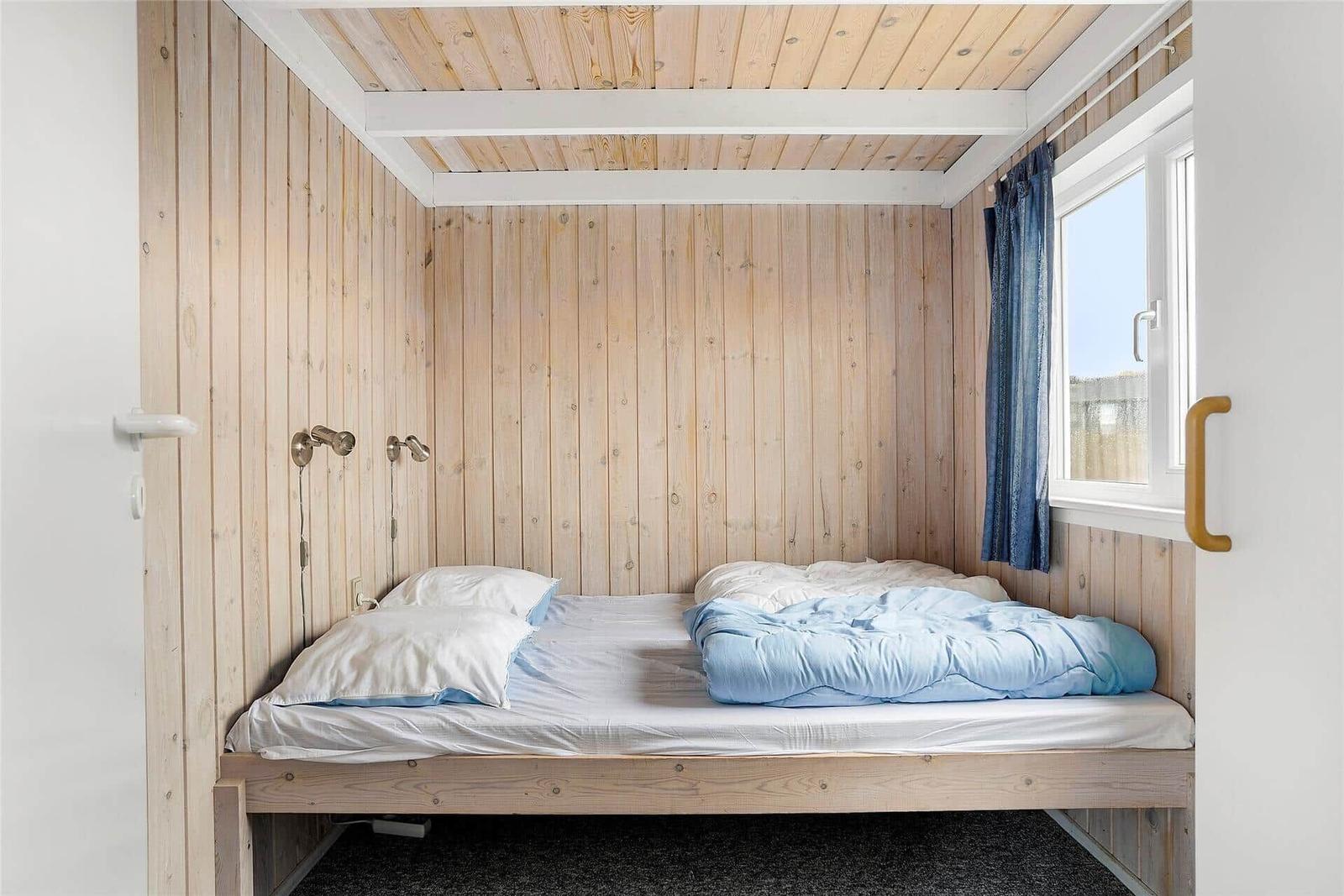 Ein Schlafzimmer mit Holzwand, Bett und Fenster mit Vorhang.