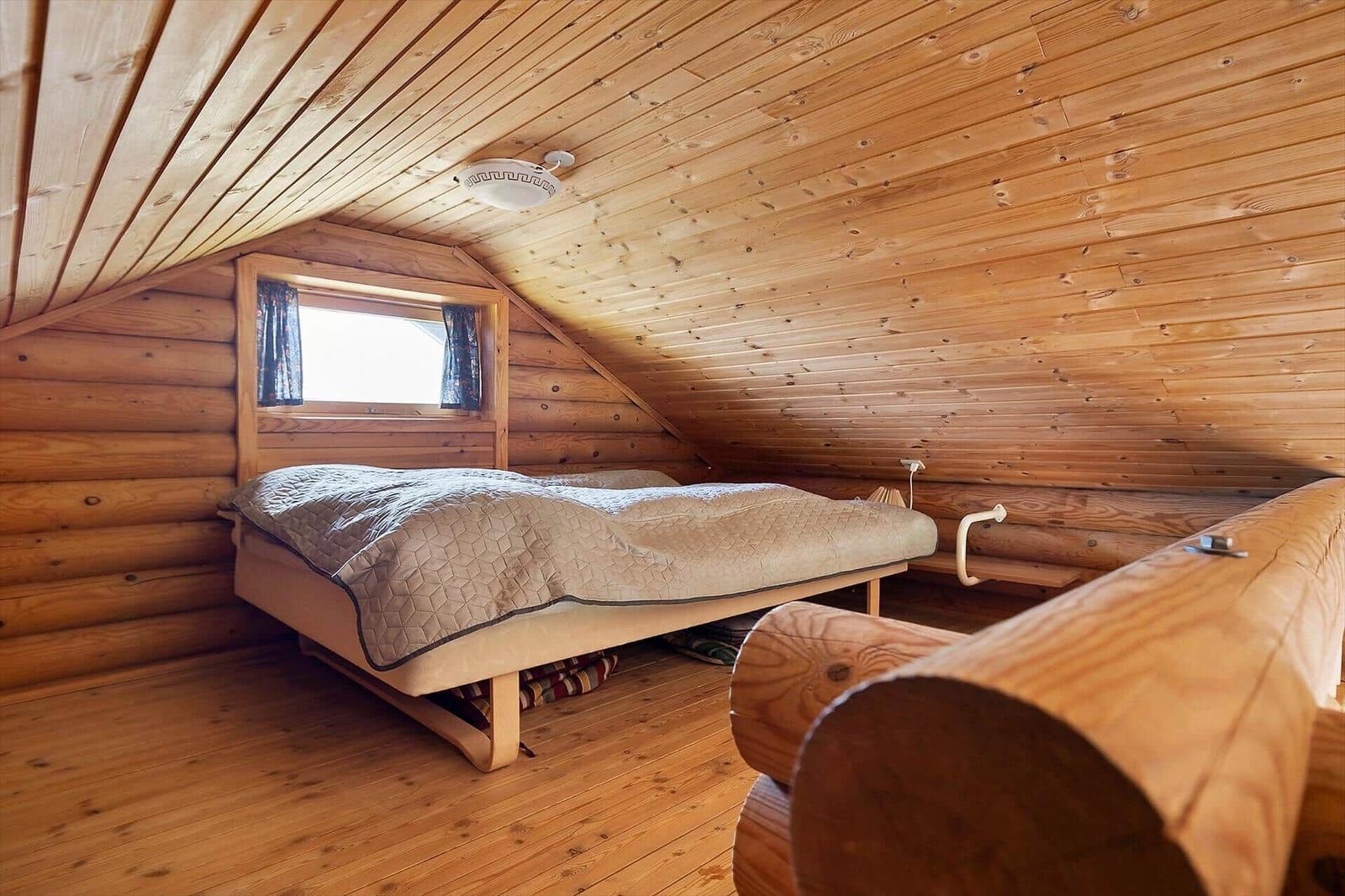 Schlafzimmer mit Holzwand, Bett und Fenster unter Dachschräge