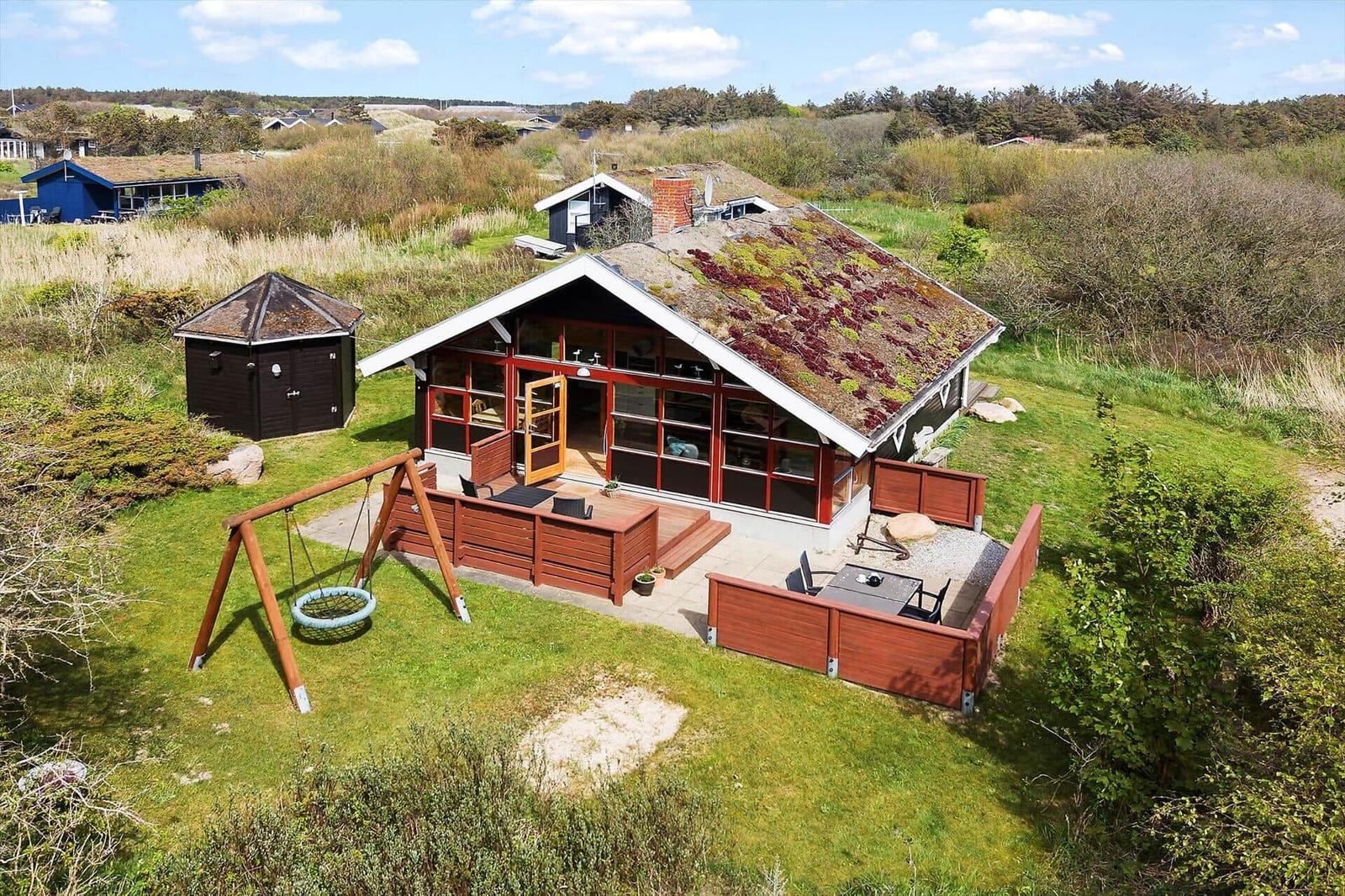 Holzhütte mit begrüntem Dach, Terrasse und Schaukel im Grün.