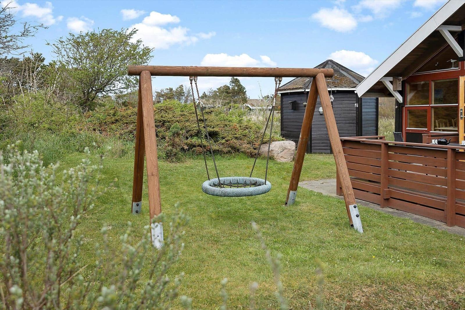 Holzschaukel im Garten neben einem Haus mit Terrasse.