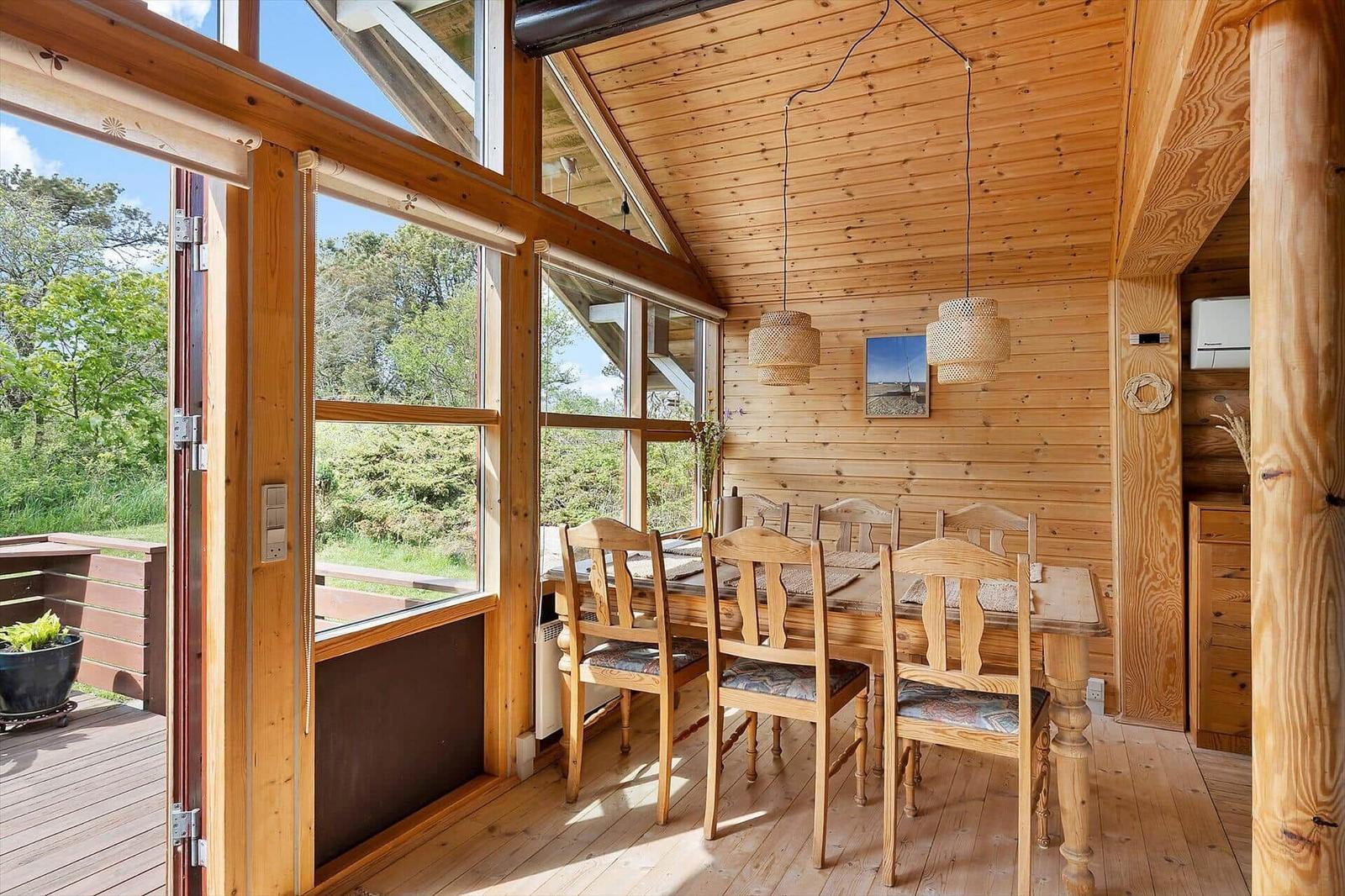 Esszimmer mit Holztisch, Stühlen und großen Fenstern zur Außenterrasse.