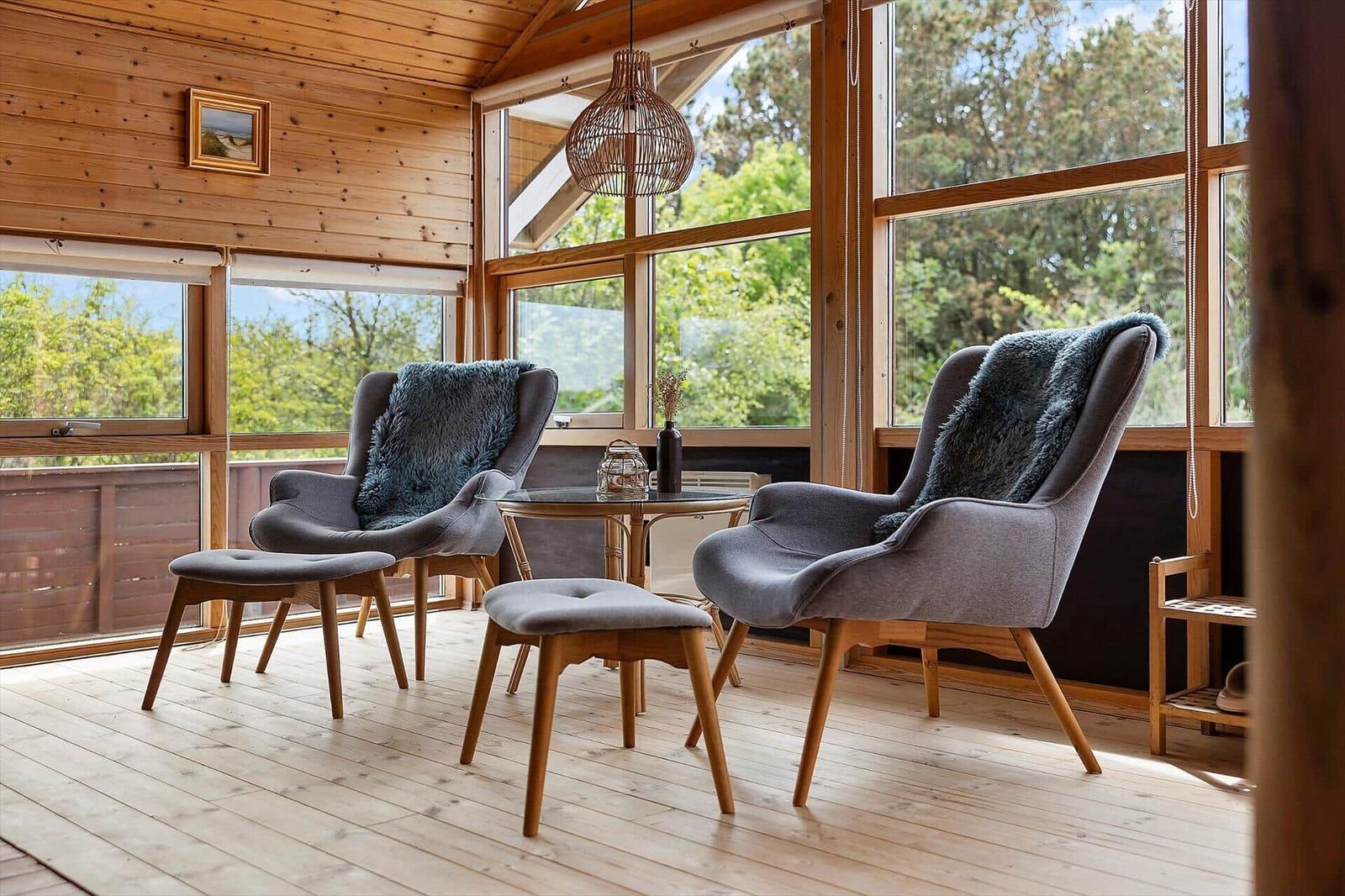 Zwei graue Sessel mit Felldecken stehen um einen runden Tisch herum. Holzfußboden und große Fenster.