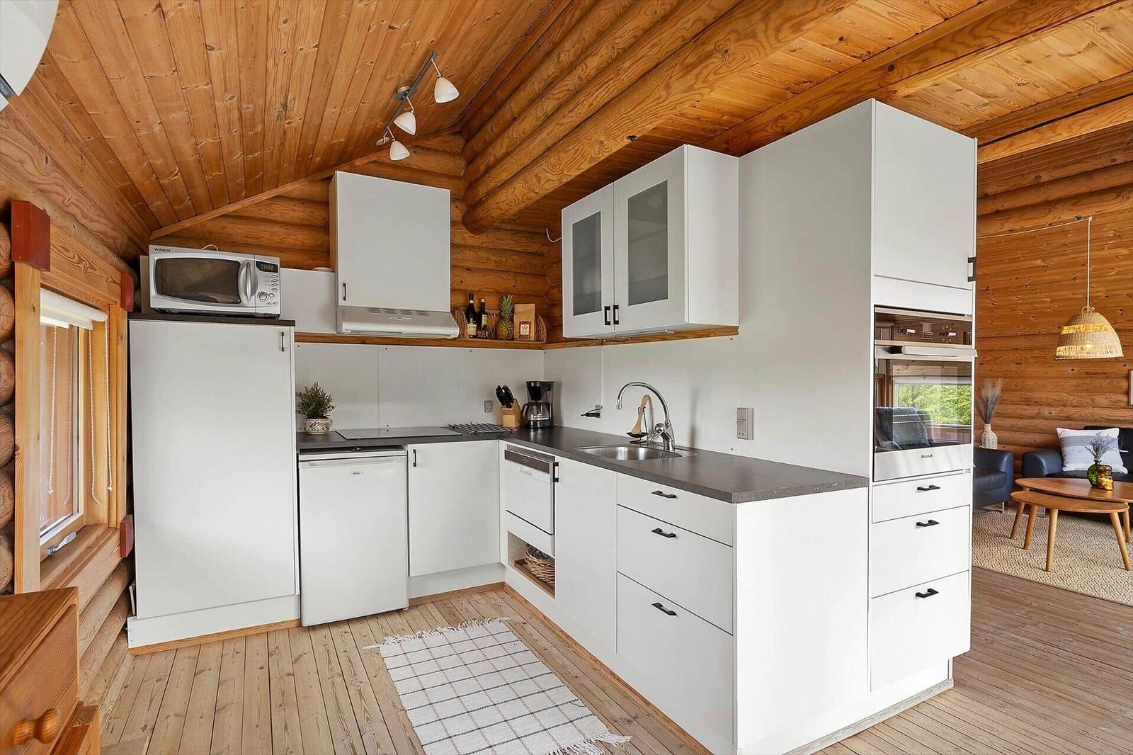 Küche mit weißen Schränken, Holzdecke und Blick in Wohnzimmer.