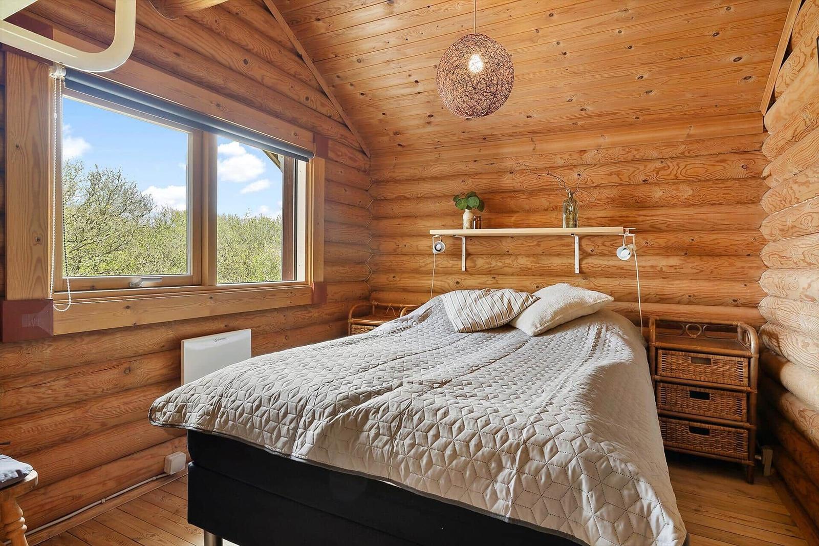 Schlafzimmer mit Holzwand, Bett, Fenster und Wandleuchten.