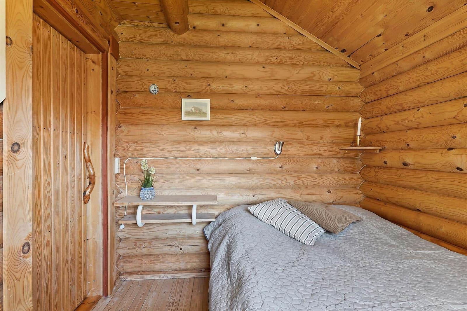 Schlafzimmer mit Holzwand, Bett und kleinem Schreibtisch.