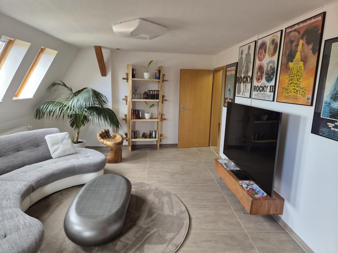 Wohnzimmer mit Sofa, TV, Bücherregal und Fenstern