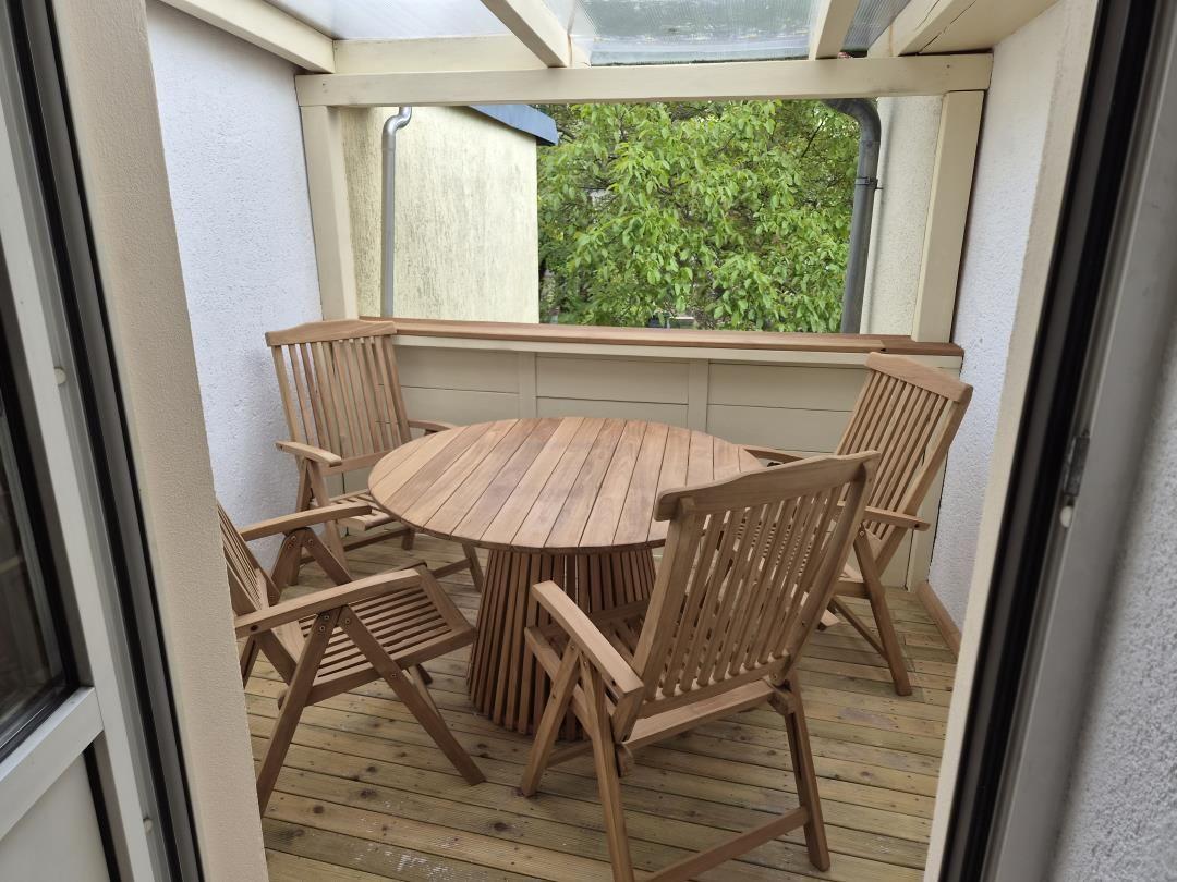 Terrasse mit runden Tisch und vier Holzstühlen, Blick auf grüne Bäume.