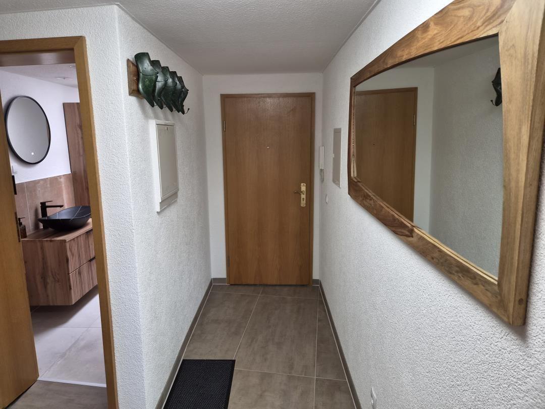 Flur mit Holztür, Spiegel und Blick in das Badezimmer mit Waschtisch.