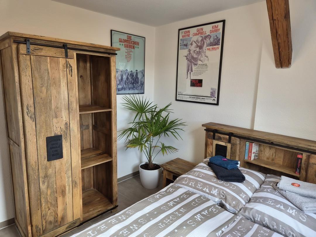 Schlafzimmer mit Holzschrank, Bett und Wandposter.