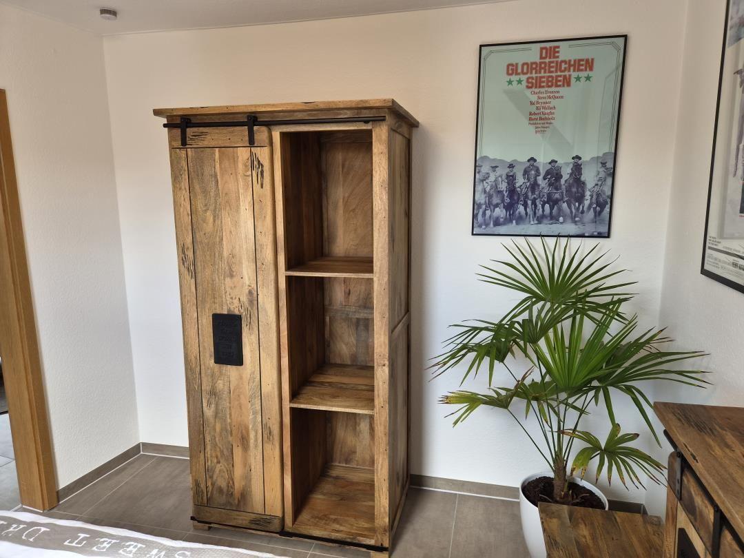Holzschrank mit Schiebetüren, Pflanze und Poster an der Wand.