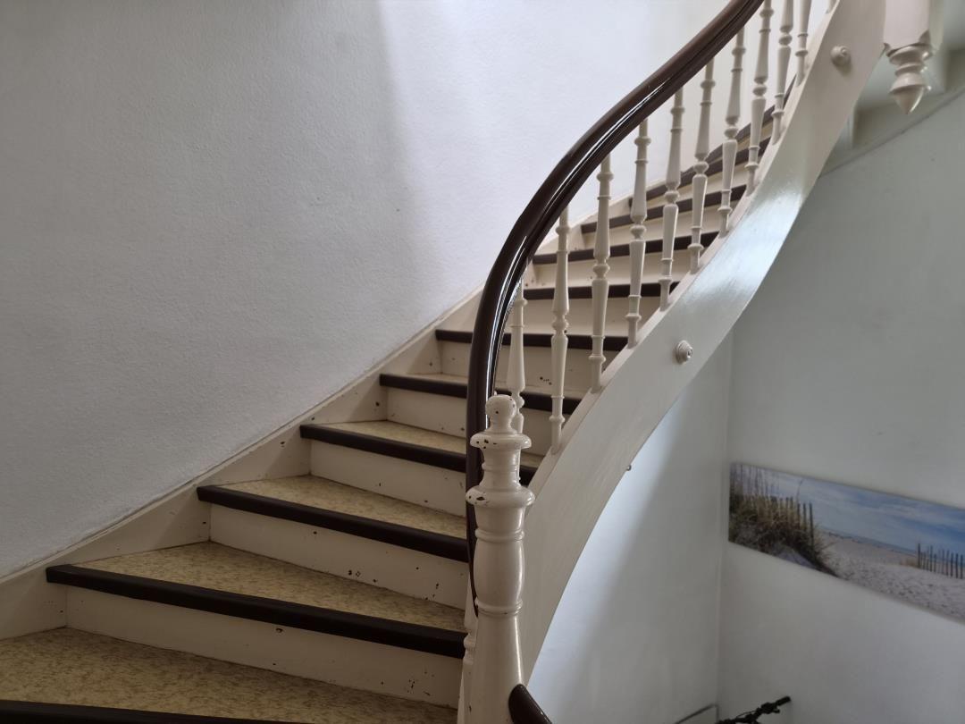 Eine Treppe mit weißer Balustrade und dunklem Geländer führt nach oben.