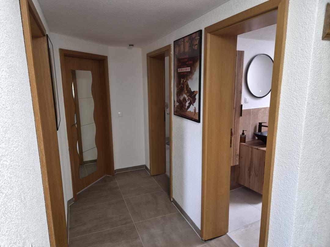 Flur mit Holztüren und Wandbild. Blick in Bad mit runden Spiegel.