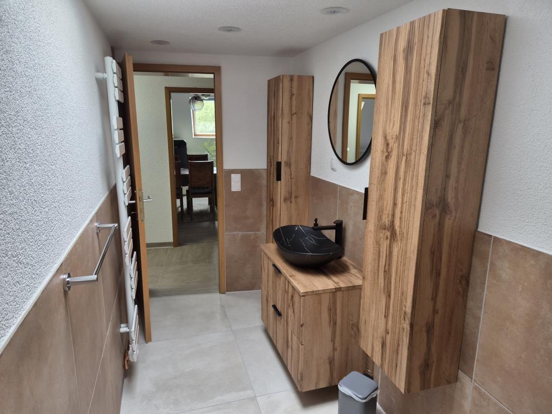 Bad mit Holzschrank, schwarzer Waschschale und runder Spiegel. Durchgang zu Esszimmer.