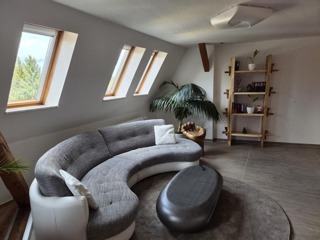 Wohnzimmer mit halbrundem Sofa, Dachfenstern und Holzregal.