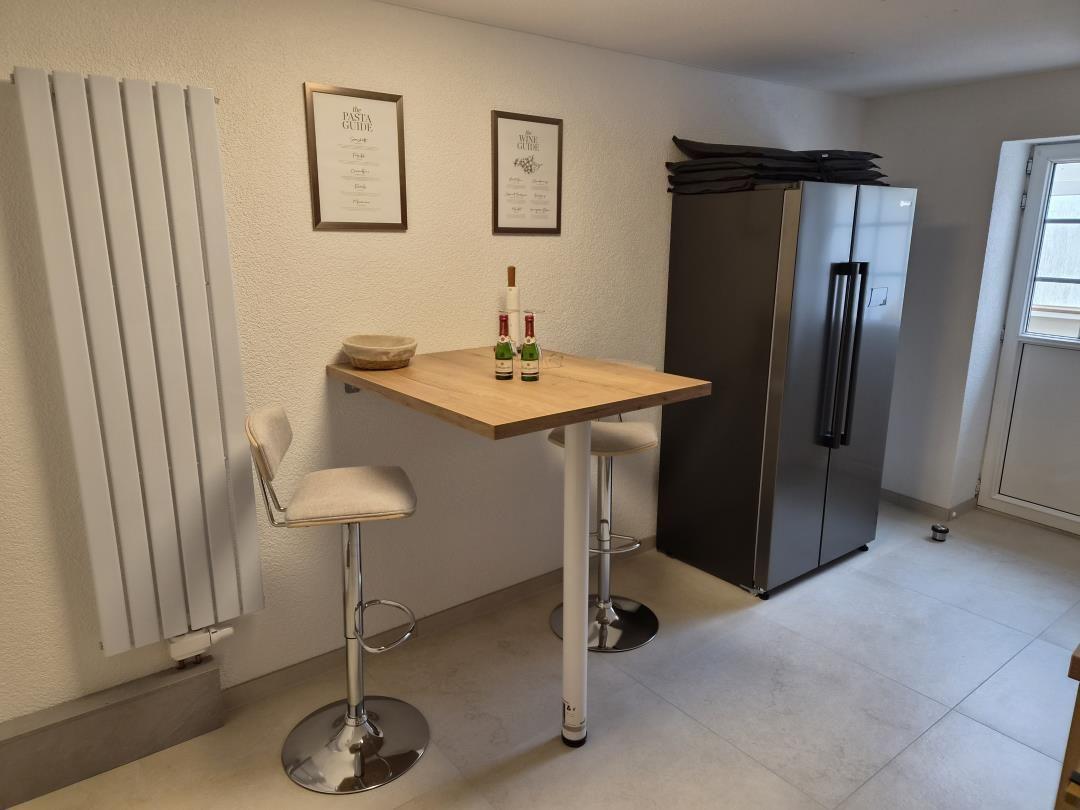 Küchenbereich mit Barhocker, Kühlschrank und Wandheizung.