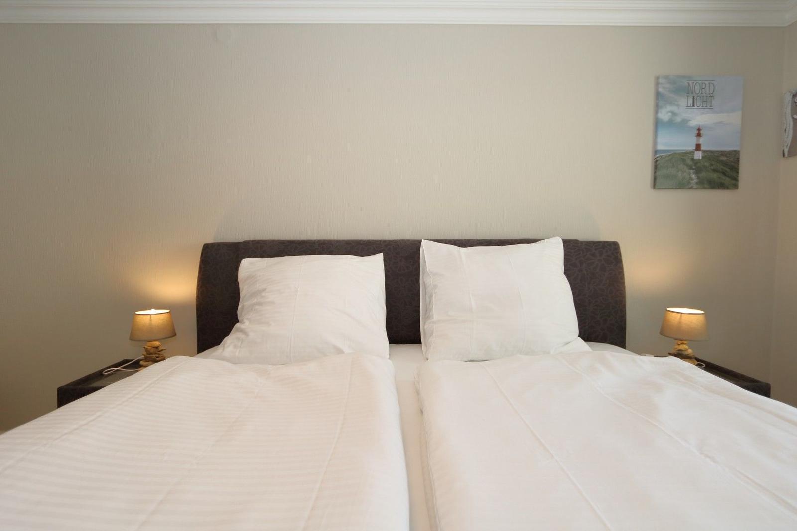 Two beds with white bedding, nightstands with lamps, and wall picture with lighthouse.