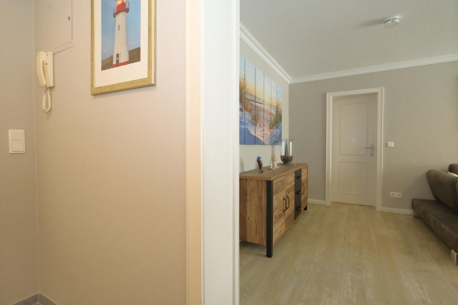 Hallway with wall art and door to living room with wooden cabinet and sofa.