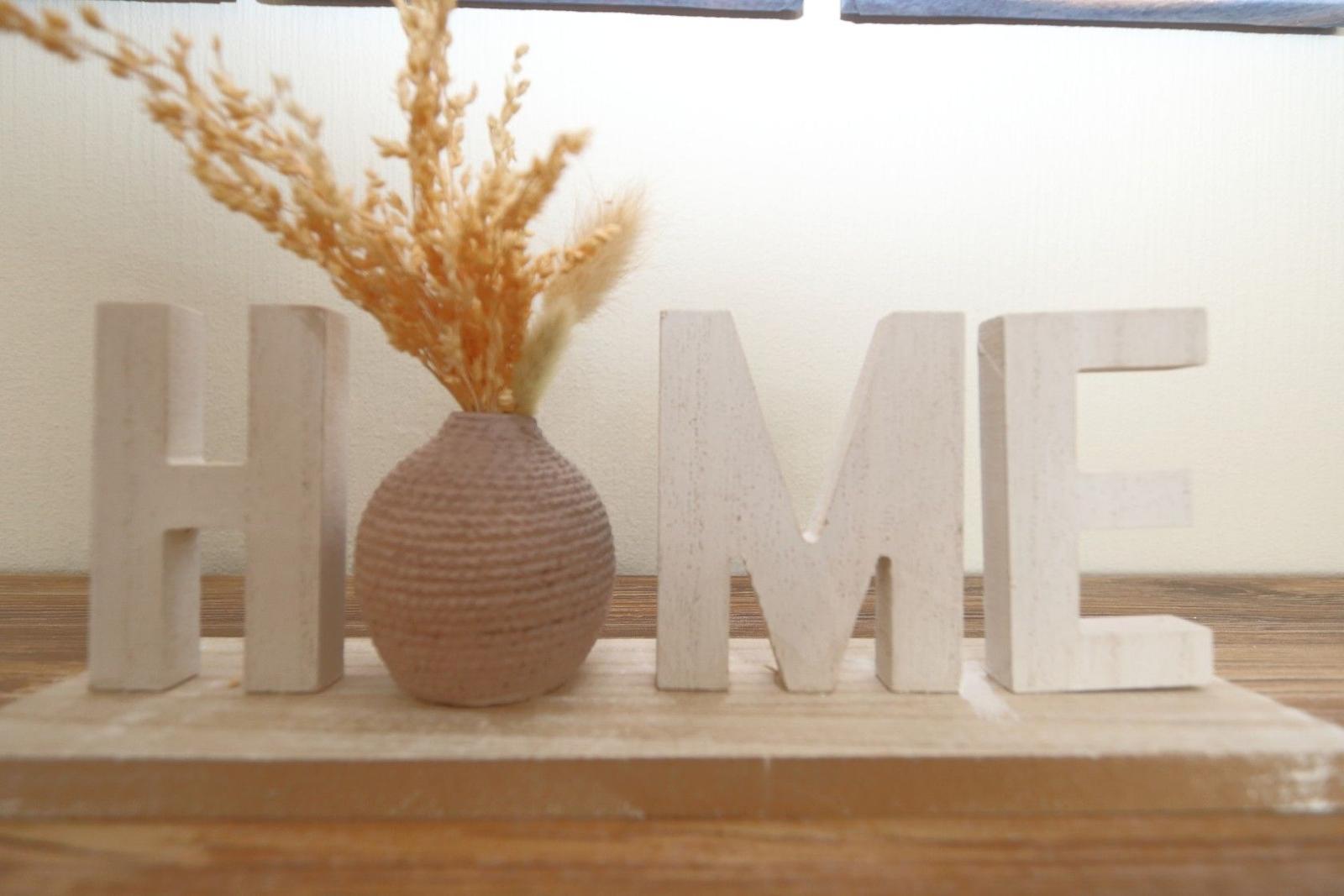 Wooden letters spelling HOME and a vase with dried plants on a wooden surface.