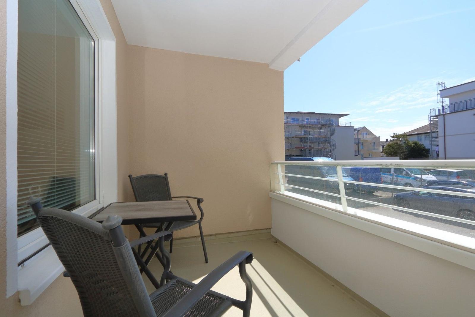 Balcony with table and two chairs, view of parking lot and buildings.