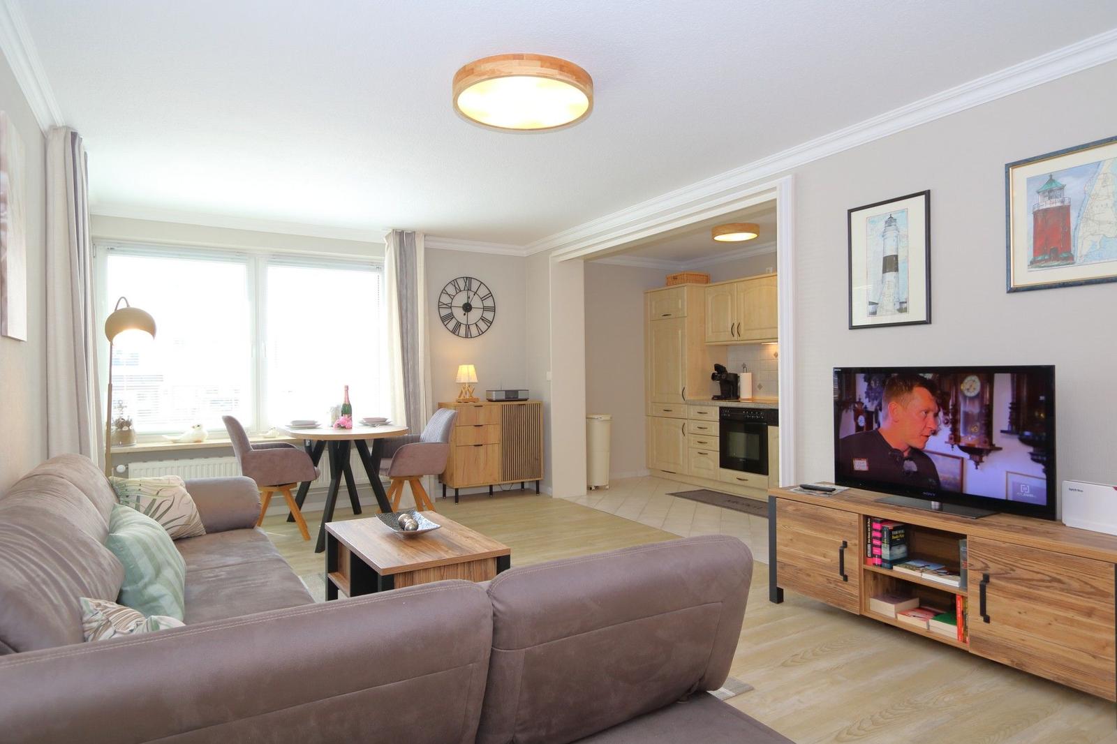 Living room with sofa, TV, and kitchen area in the background.