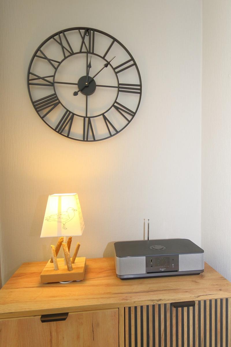 Wooden cabinet with lamp and radio under a wall clock.