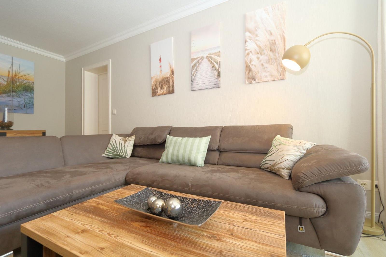 A living room with a brown sectional sofa, a wooden table, and wall art.