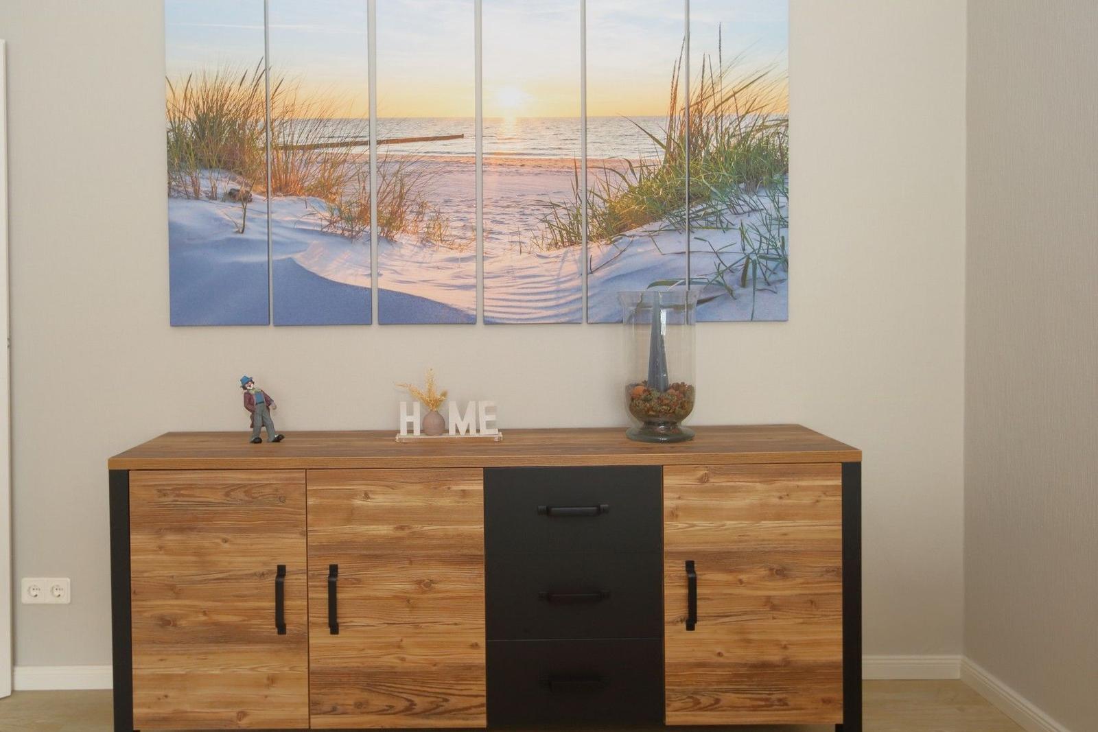 Cabinet with wooden top and black drawers. Wall picture shows beach at sunset.