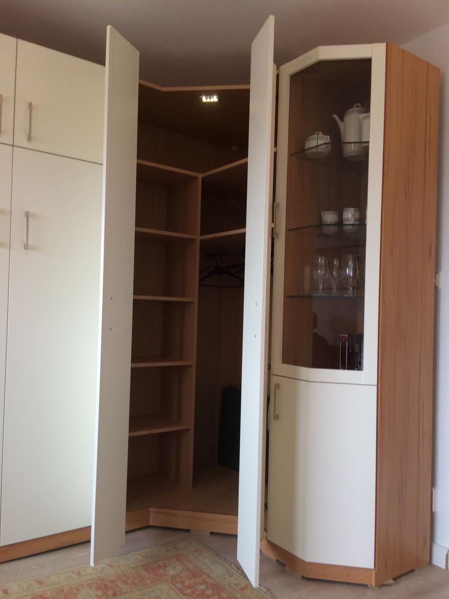 Glasvitrine mit Geschirr und Gläsern neben einem Kleiderschrank mit offenen Türen.