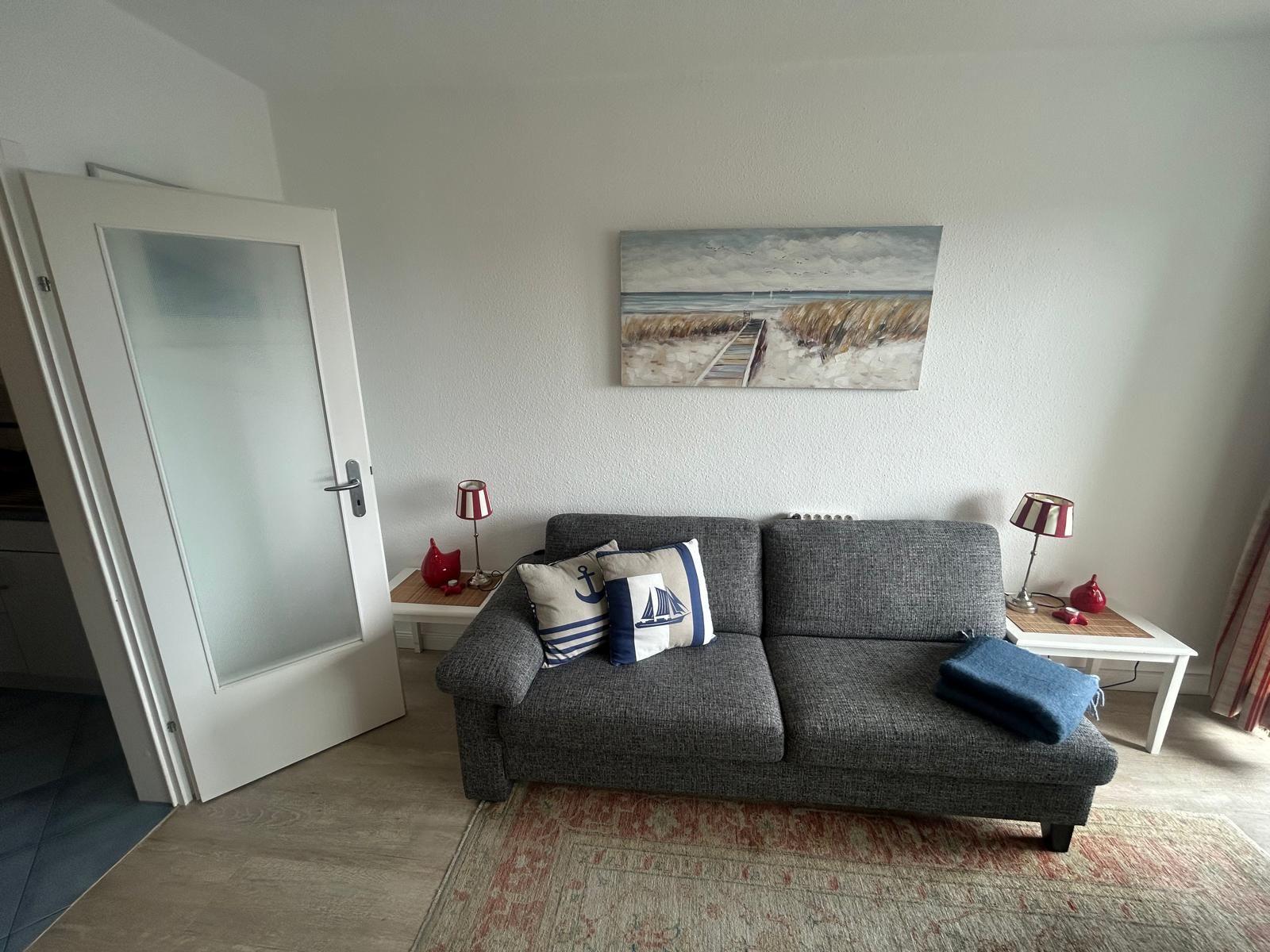 Ein Wohnzimmer mit grauem Sofa, zwei Beistelltischen und einem Wandbild.