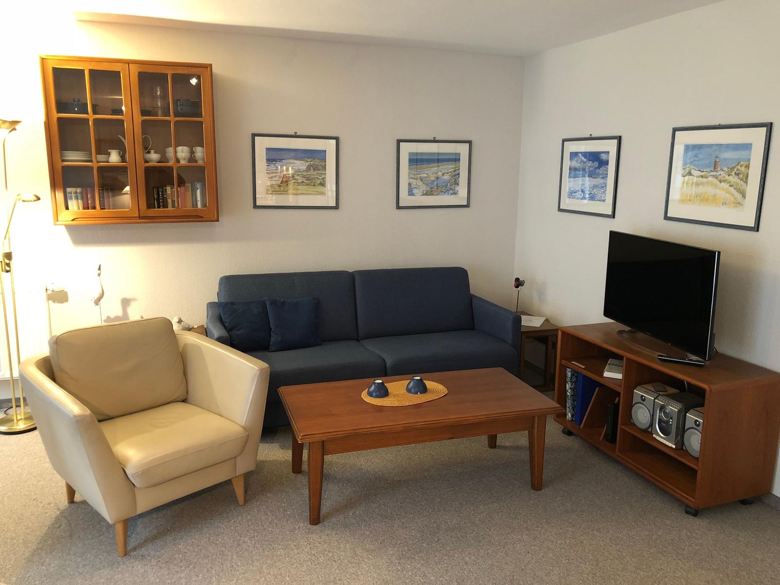 Wohnzimmer mit Sofa, Sessel, Couchtisch und Fernseher.