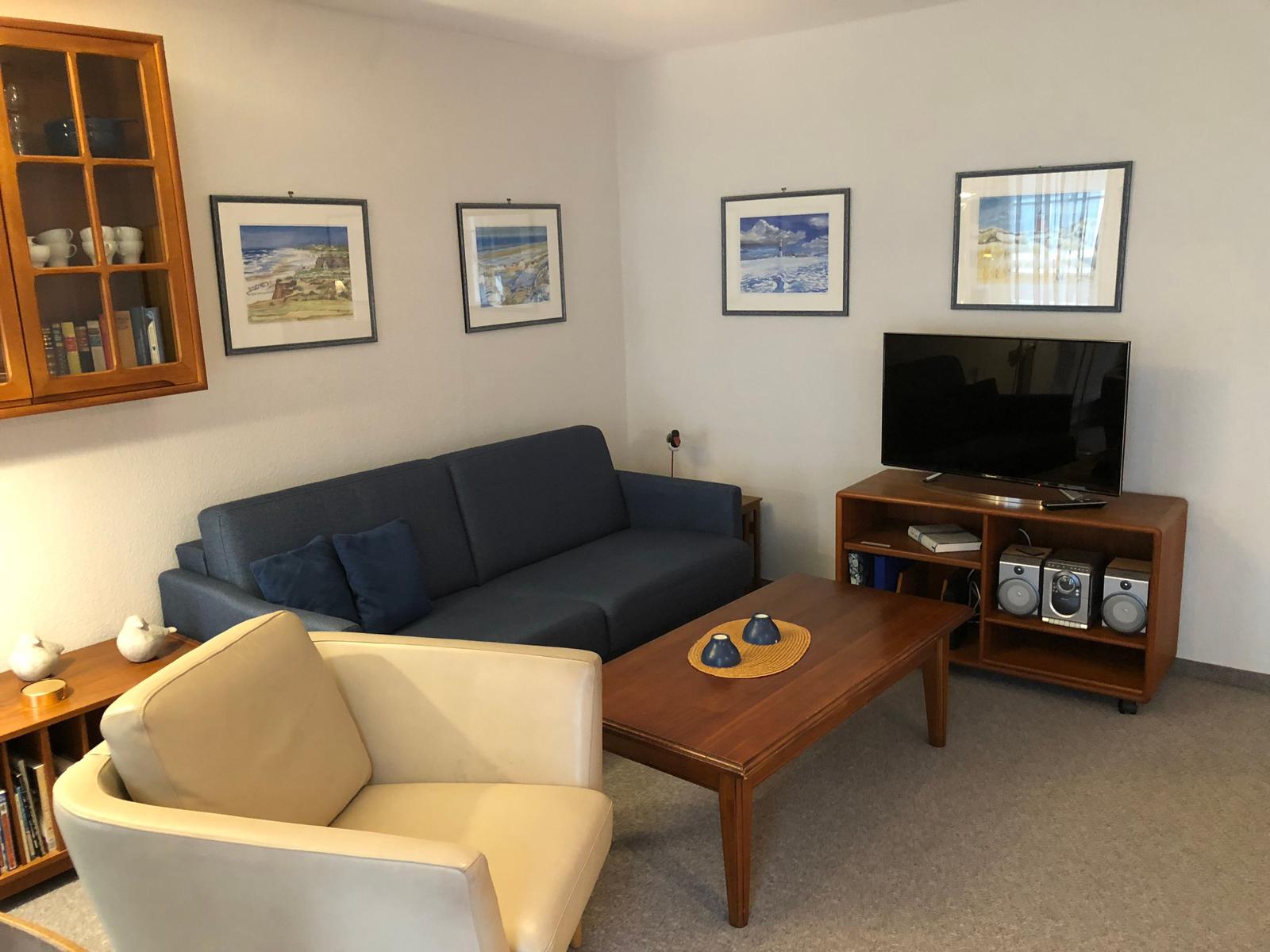 Ein Wohnzimmer mit Sofa, Sessel, Couchtisch und Fernseher.
